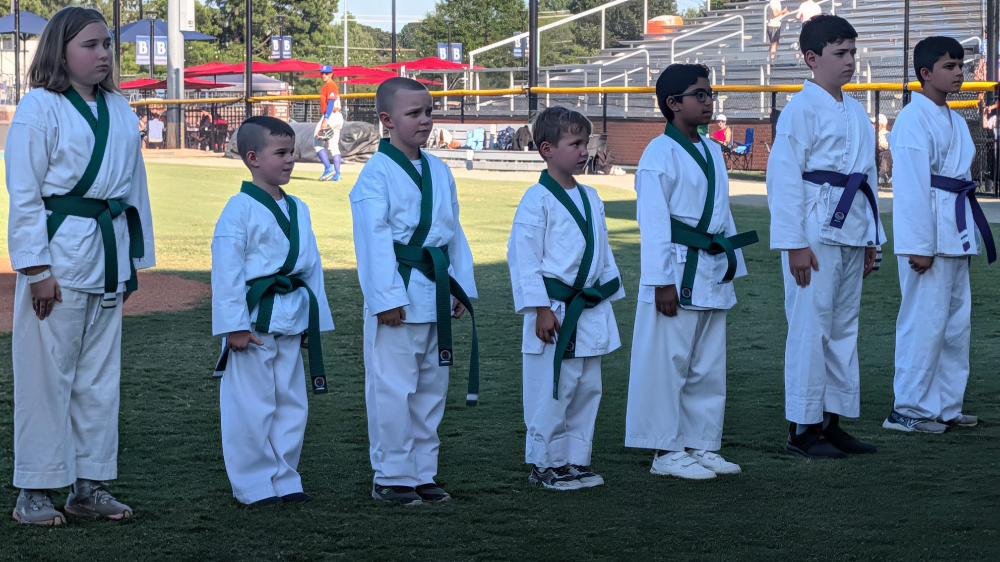 Young green belt and purple belt students standing at attention on the outfield grass.