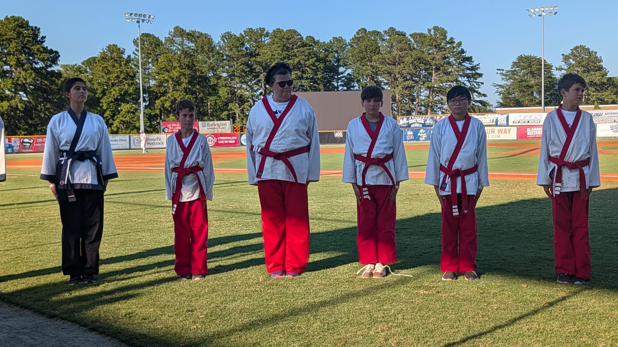 Karate USA red belt students standing at attention in the evening light at Burlington Athletic Stadium.