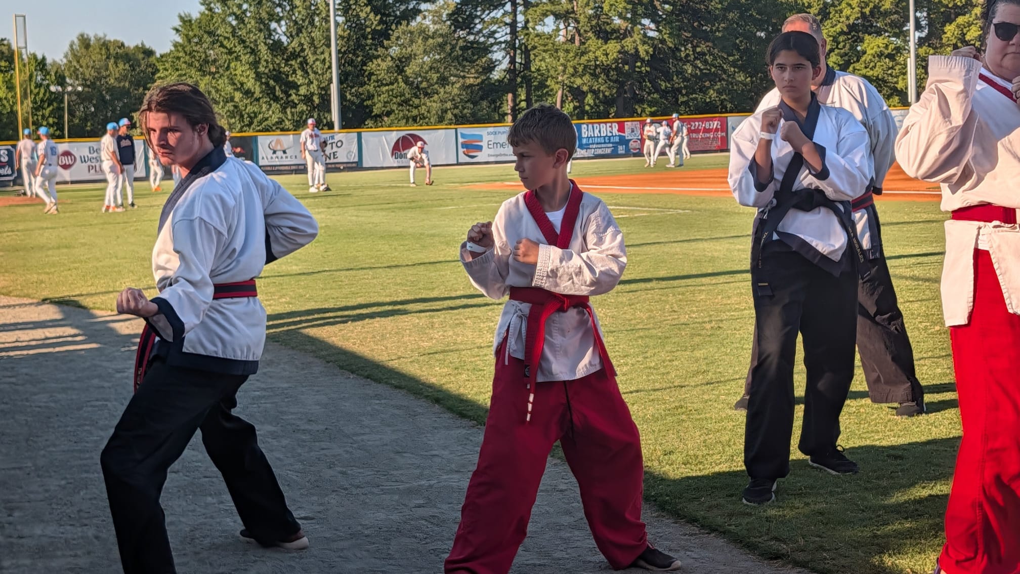 Three Karate USA students holding a fighting stance on the field while the Sock Puppets warm up behind them.